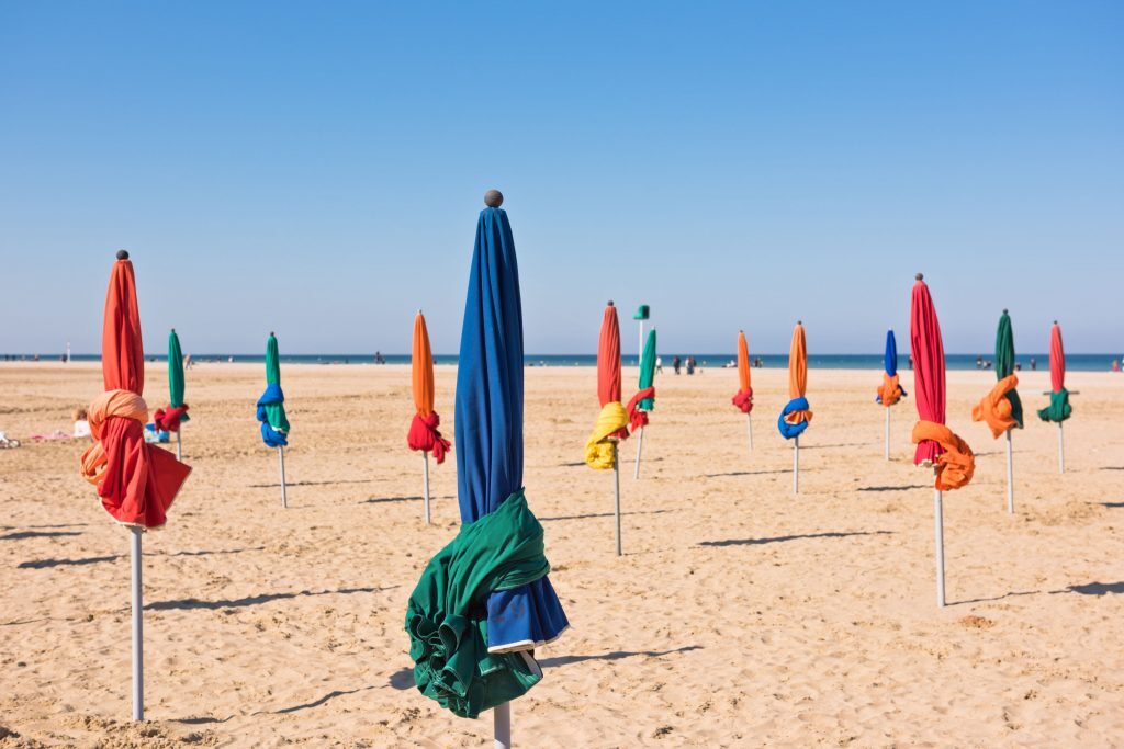 Deauville plage et ses fameux parasols lors d'une journée bien ensoleillée avec un ciel bleu, à visiter lors de votre week-end en couple en Normandie
